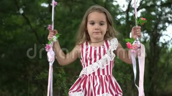 美丽的小女孩穿着裙子骑着秋千在公园里在大自然中视频的预览图