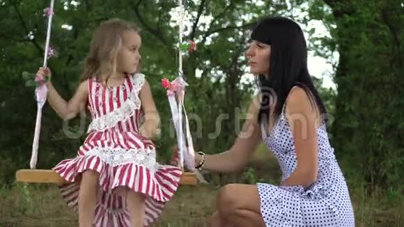 美丽的小女孩和她的母亲骑在秋千上在公园里在大自然中视频的预览图