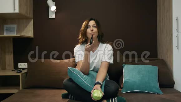 女人看电视吃苹果坐在卧室的床上用遥控器切换通道视频的预览图