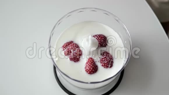 特写镜头雌性的手把草莓放在牛奶中的透明杯子里作为搅拌机视频的预览图
