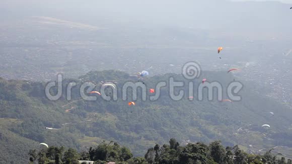 乘坐彩色降落伞的滑翔伞在绿色的山谷中飞过城市视频的预览图