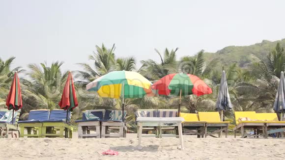 在绿棕丛林的背景下沙滩床在五颜六色的雨伞下视频的预览图