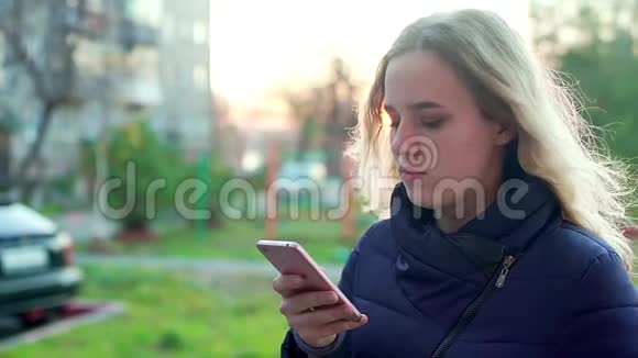 一个年轻漂亮的女孩站在街上手里拿着一部智能手机视频的预览图