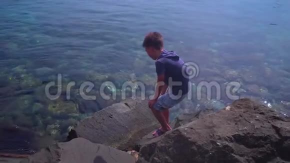 男孩在海滨攀爬天然石头和岩石找螃蟹视频的预览图