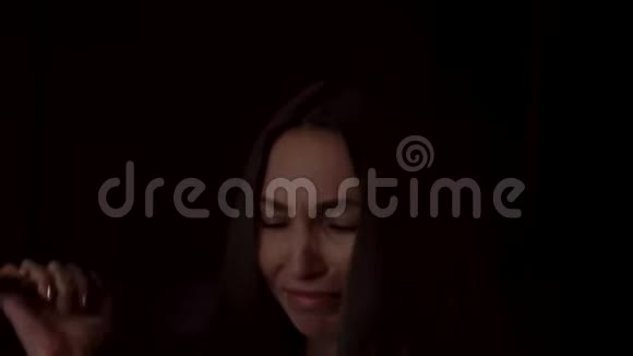 一个悲伤的年轻女子抱着膝盖在黑暗的背景下哭泣的肖像孤独的概念抑郁的女性视频的预览图