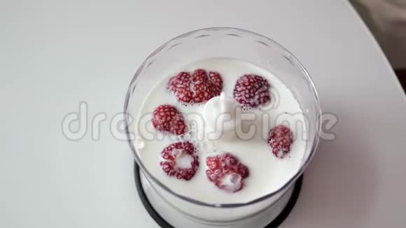 特写镜头雌性的手把草莓放在牛奶中的透明杯子里作为搅拌机视频的预览图