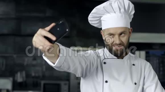 专业厨师在厨房摆姿势厨师用手机拍自拍照片视频的预览图