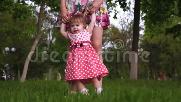 妈妈教小女儿在绿色草坪上的夏天公园散步视频的预览图