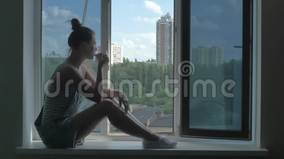 迷人的女人坐在窗台上用咖啡欣赏户外风景视频的预览图