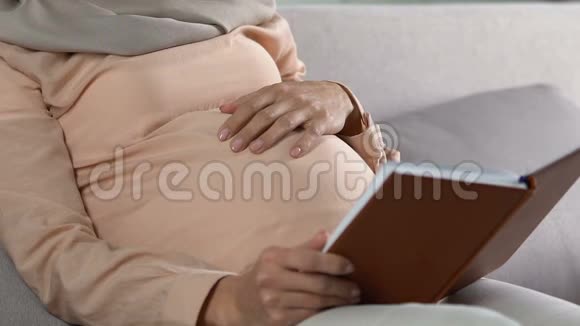 母亲温柔地抚摸着肚子给未来的孩子看书照顾孩子视频的预览图