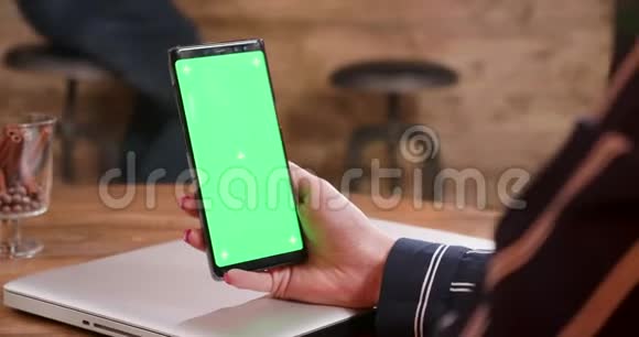 一个年轻的女人手里拿着绿色屏幕的智能手机视频的预览图