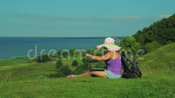 一位背着背包坐在山边俯瞰湖面的女士打开了一张笔记本电脑的指纹视频的预览图