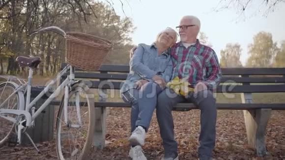一张快乐的退休白人夫妻在阳光下坐在长凳上说话的肖像成熟的欧洲视频的预览图