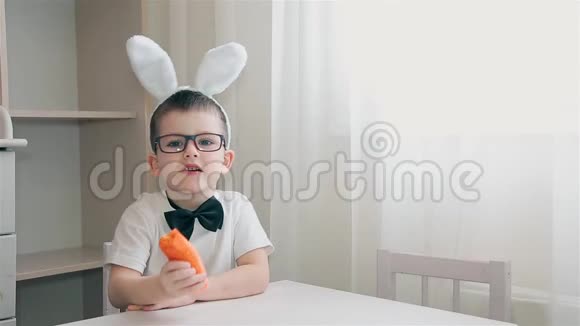 一个长着兔子耳朵的男孩坐在白色的桌子旁吃胡萝卜视频的预览图