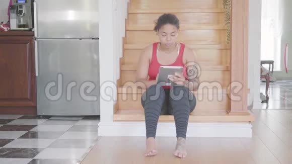漂亮的非裔美国女人坐在大房子一楼的楼梯上在她的平板电脑上发短信女孩视频的预览图