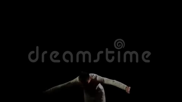 穿着白色衣服黑色背景的英俊男体操运动员在蹦床上缓慢地跳跃表演翻转和跳跃视频的预览图