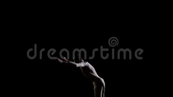 穿着白色衣服黑色背景的英俊男体操运动员在蹦床上缓慢地跳跃表演翻转和跳跃视频的预览图