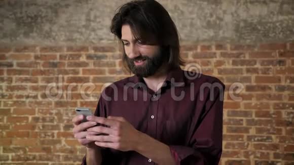 年轻漂亮的黑发男子留着胡子正在看智能手机上的照片笑砖背景交流观念视频的预览图