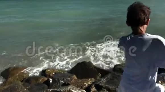 赤脚男孩在海边的大石头边跳着跑视频的预览图