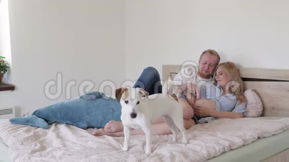 年轻的一家人在卧室的床上等待一个婴儿一个男人和一个孕妇在床上玩耍视频的预览图