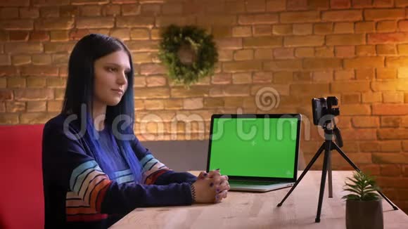 年轻时尚的高加索女性视频博客作者的特写肖像用一台带有绿色笔记本电脑在镜头上直播视频的预览图