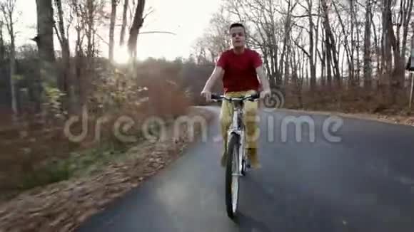 少年骑自行车在阳光明媚的秋林路上骑脚踏车视频的预览图