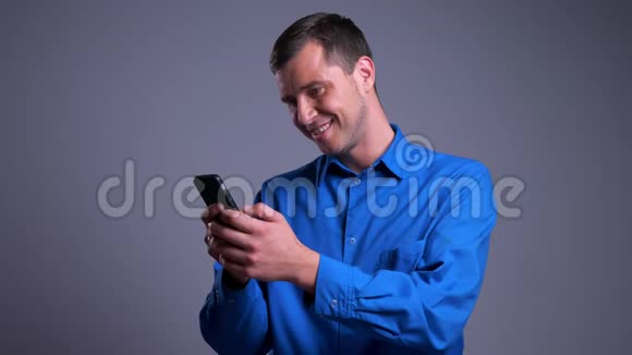 一张快乐的白种人成年男子在手机上打字并在镜头前微笑的特写照片视频的预览图