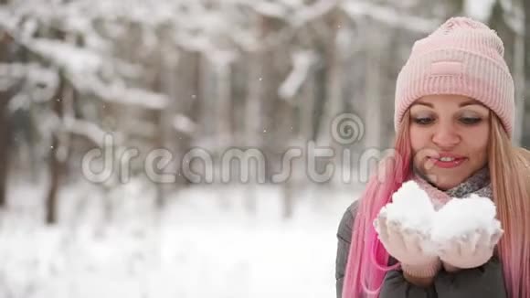 动作缓慢一个穿着夹克帽和围巾的女人在冬天的森林里手里拿着雪吹进视频的预览图
