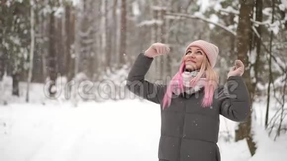 动作缓慢一个穿着夹克帽和围巾的女人在冬天的森林里手里拿着雪吹进视频的预览图