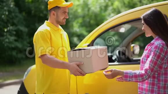 穿黄色制服的送货员给汽车附近的女顾客送包裹视频的预览图