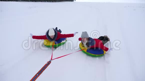 快乐的孩子们在冬天雪橇一个充气的雪管挥动他们的手孩子们又笑又高兴女孩视频的预览图