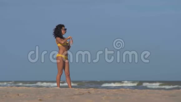 阳光下的女人从海滩上的玻璃瓶中喝水视频的预览图