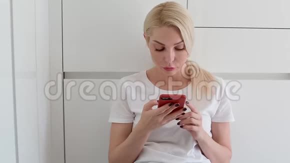 年轻的白人妇女坐在地板上使用智能手机视频的预览图