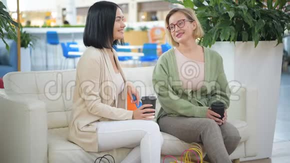 两位美丽的年轻女士在商场购物后休息和讨论一些事情喝着外卖咖啡视频的预览图