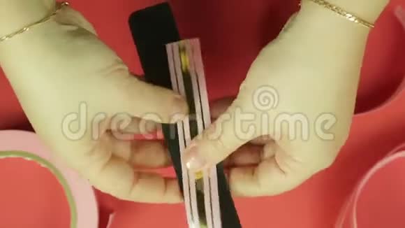女人手正在模板上包裹一条粉红色的丝带用来做礼物蝴蝶结红色背景视频的预览图