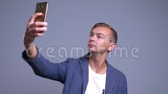年轻白种人在手机上自拍的特写照片背景是灰色的视频的预览图