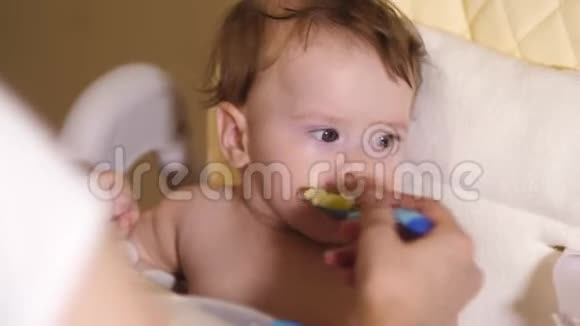 妈妈用勺子喂宝宝午餐给孩子吃美味的水果泥孩子坐在婴儿椅上喂孩子视频的预览图