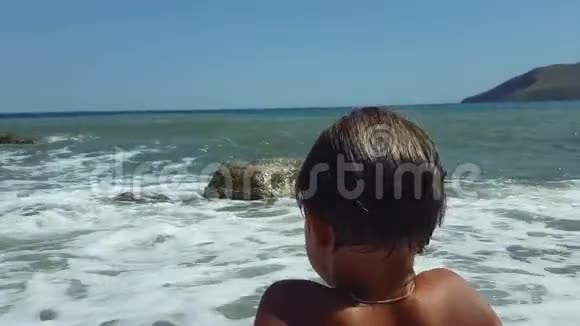 一个小男孩坐在沙滩上看着水进出视频的预览图