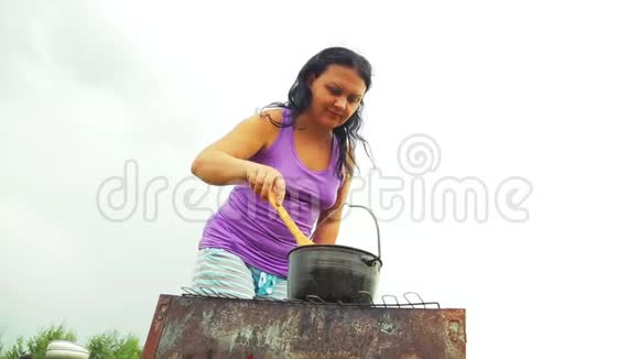 一个女人在火上用木勺在水壶里搅拌汤他远离烟雾视频的预览图