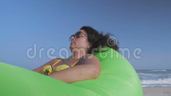美丽的女人在比基尼海上放松躺在沙滩上的绿色充气小屋视频的预览图