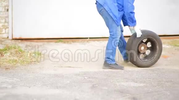 一名男子汽车修理工用圆盘在沥青汽车轮胎上滚动视频的预览图