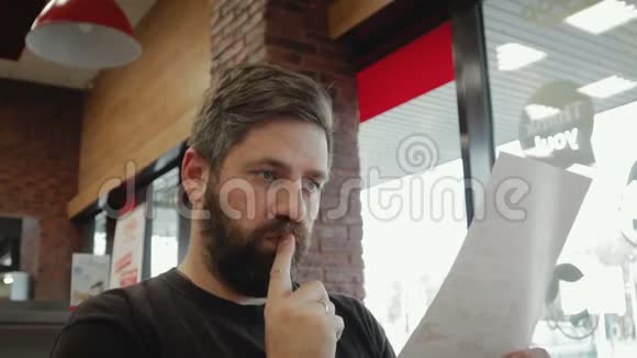 一个留着胡子的开朗的年轻人看菜单在酒吧下订单视频的预览图