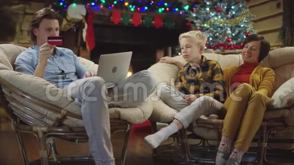 在笔记本电脑上进行帅气的网上购物而圣诞礼物则落在上面的女人和小男孩身上视频的预览图