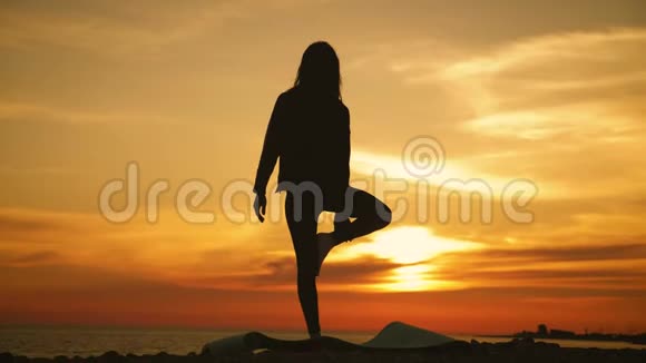 剪影年轻女子在海上日落时练习瑜伽快乐的生活时刻海滩上的剪影瑜伽视频的预览图