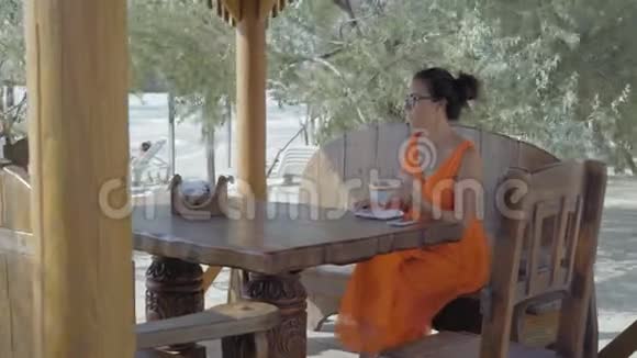 美丽的女人戴着眼镜沉思地看着大海坐在海滩上的咖啡馆里吃甜点视频的预览图