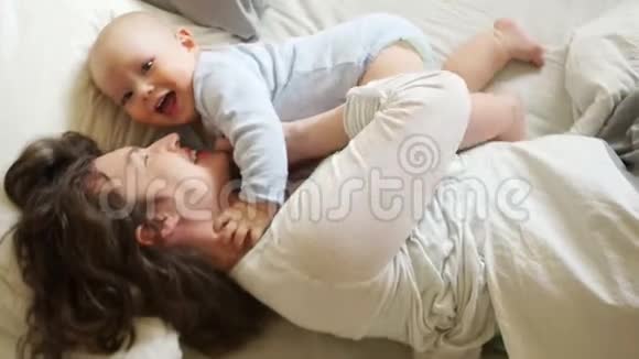 阳光家庭早晨妈妈和宝宝在床上一个女人挠痒痒拥抱她一岁的儿子母亲节视频的预览图