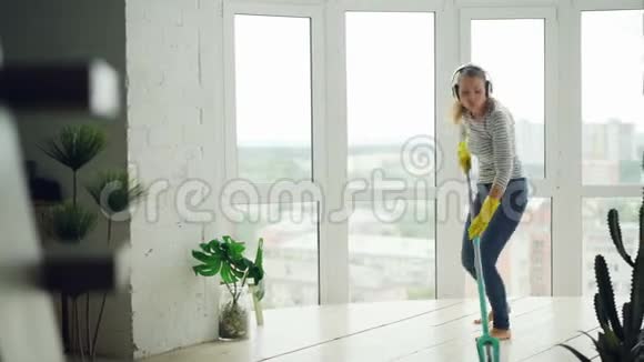 快乐的年轻女士正在做家务拖地板在耳机里享受音乐跳舞和唱歌美丽美丽视频的预览图