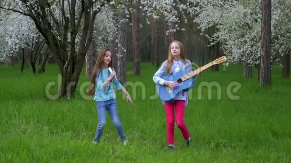 临时音乐会在森林公园快乐的小女朋友跳舞唱歌和弹吉他盛开的大树春天视频的预览图
