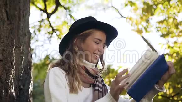 城市公园里带着漂亮围巾看书的微笑女孩的肖像画视频的预览图