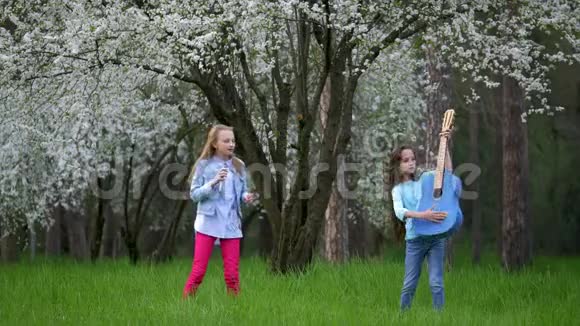 幼儿女朋友玩得开心跳舞唱歌弹蓝声吉他春天盛开的树进入公园自负自负视频的预览图